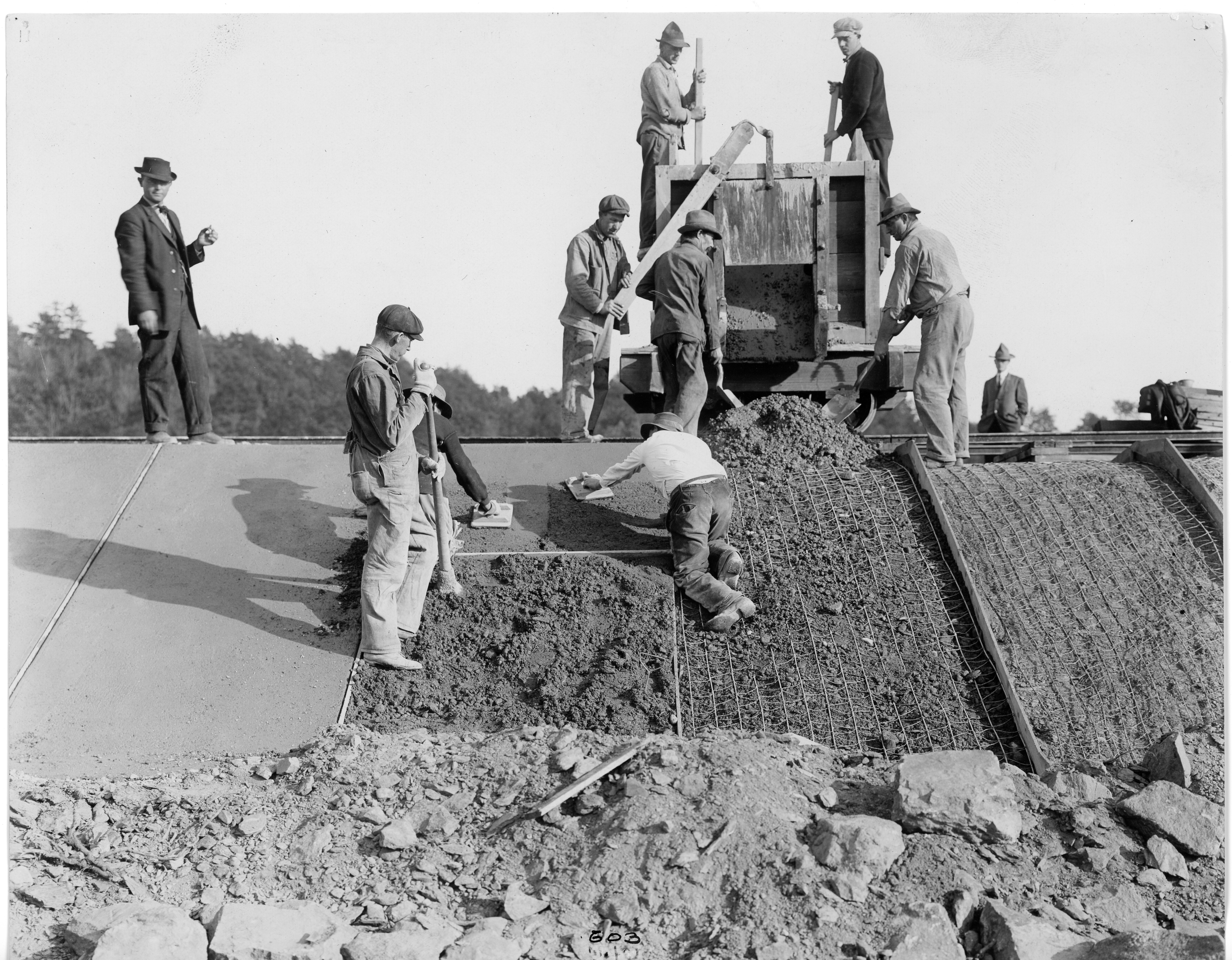 Men using machine and hand tools to apply cement to a riverbank Men using machine and hand tools to apply cement to a riverbank